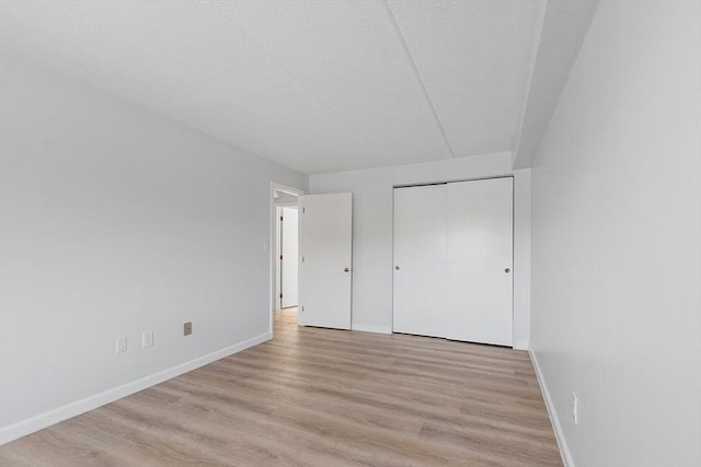 unfurnished bedroom featuring light wood-style floors, baseboards, and a closet