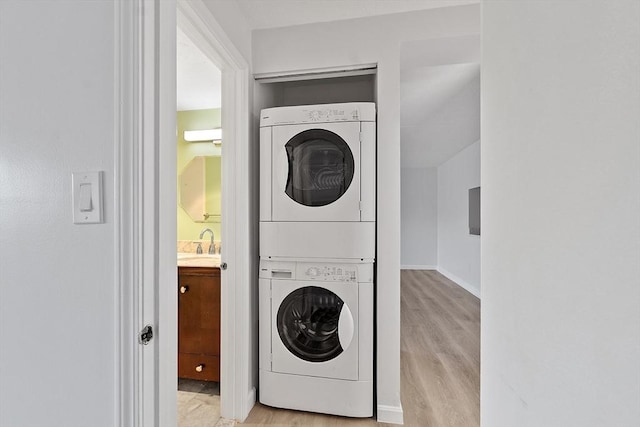 laundry area featuring laundry area, a sink, stacked washer / dryer, and wood finished floors