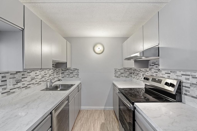 kitchen featuring a textured ceiling, under cabinet range hood, a sink, light wood-style flooring, and appliances with stainless steel finishes