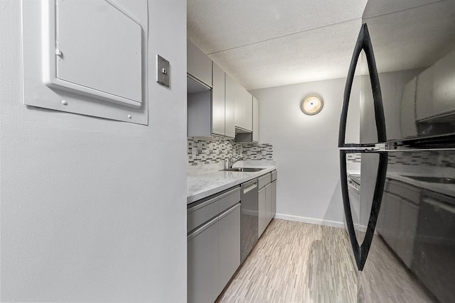 kitchen featuring a sink, light wood finished floors, backsplash, stainless steel dishwasher, and gray cabinetry