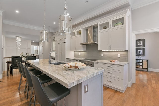 kitchen with wall chimney exhaust hood, a center island with sink, sink, and white cabinetry