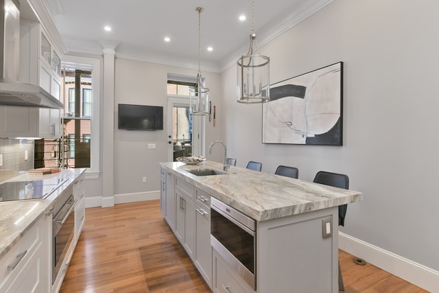 kitchen with a center island with sink, a kitchen breakfast bar, wall chimney range hood, backsplash, and appliances with stainless steel finishes