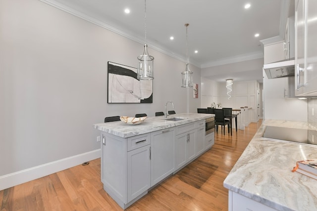 kitchen with a kitchen island with sink, light hardwood / wood-style flooring, hanging light fixtures, and black electric cooktop