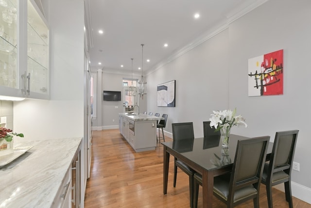 dining space featuring sink, light hardwood / wood-style flooring, and crown molding