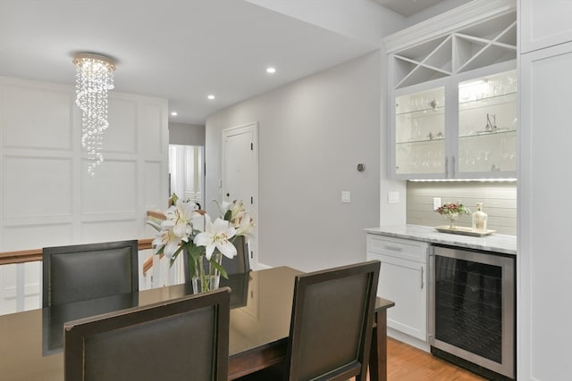 dining room featuring bar area, beverage cooler, a notable chandelier, and light hardwood / wood-style floors