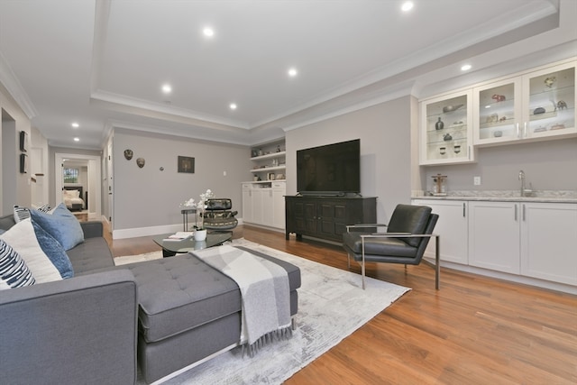 living room with light wood-type flooring, a tray ceiling, indoor wet bar, and crown molding