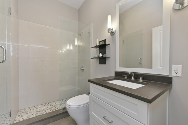 bathroom featuring toilet, vanity, tile patterned flooring, and a shower with shower door