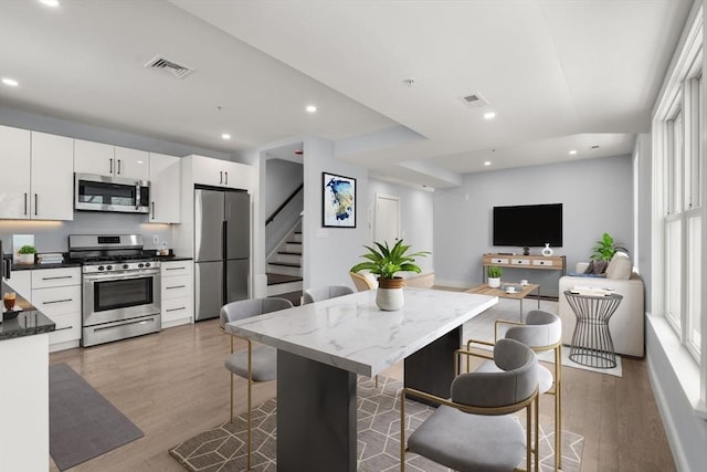 167 Charles St, Waltham, MA 02453 - kitchen featuring appliances with stainless steel finishes, light wood-style floors, recessed lighting, white cabinetry, and a kitchen bar