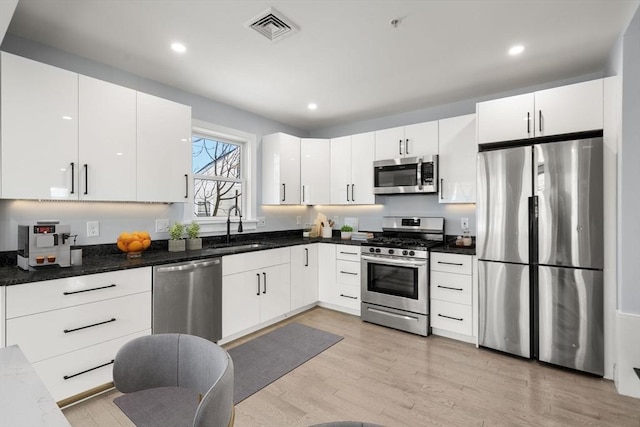 167 Charles St, Waltham, MA 02453 - kitchen featuring appliances with stainless steel finishes, a sink, white cabinetry, light wood finished floors, and dark stone counters