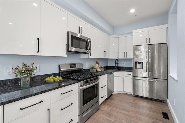 167 Charles St, Waltham, MA 02453 - kitchen with stainless steel appliances, white cabinets, light wood-type flooring, dark stone counters, and a sink
