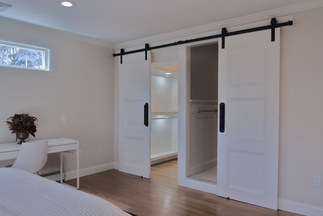 unfurnished bedroom featuring ornamental molding, wood finished floors, baseboards, and a barn door