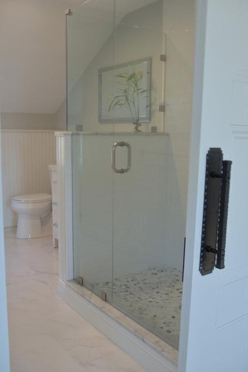 bathroom with a stall shower, wainscoting, toilet, marble finish floor, and vaulted ceiling