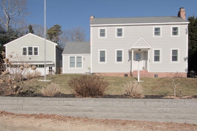 colonial-style house featuring crawl space, a shingled roof, a chimney, and a front yard