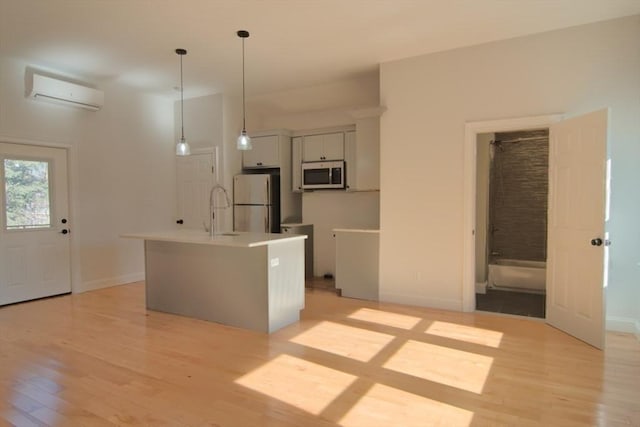 kitchen with stainless steel microwave, light wood-type flooring, a wall unit AC, and freestanding refrigerator