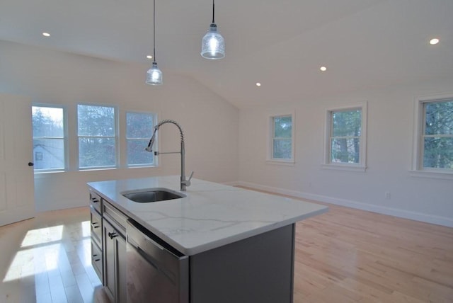 kitchen featuring light wood finished floors, dishwasher, hanging light fixtures, a kitchen island with sink, and a sink