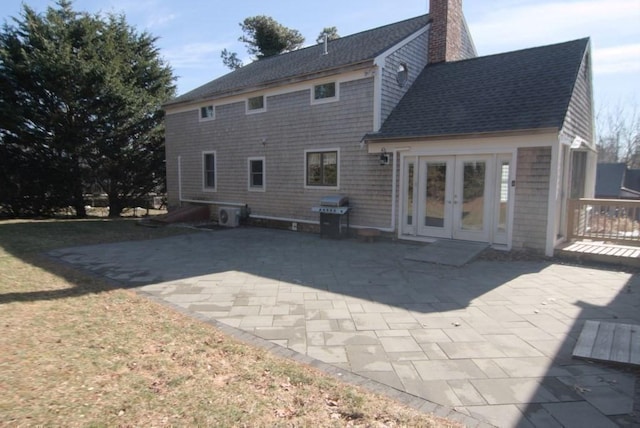 back of house with a patio area, roof with shingles, a chimney, and french doors