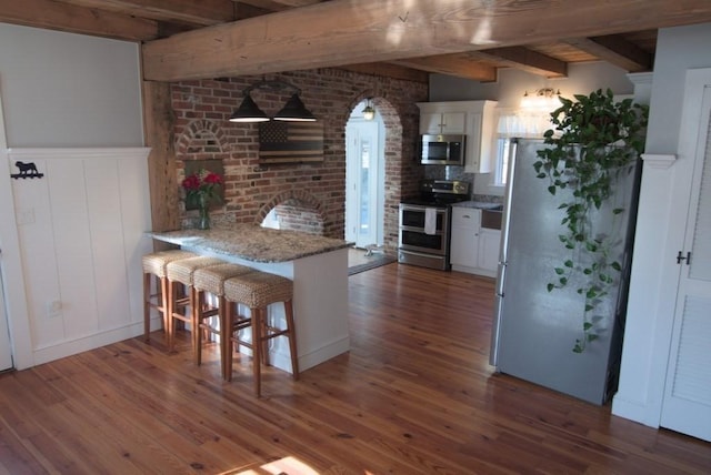 kitchen featuring stainless steel appliances, wood finished floors, beam ceiling, and white cabinetry