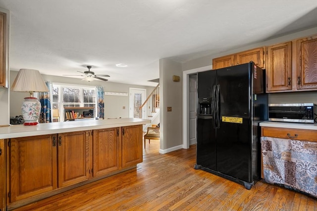 kitchen featuring black fridge with ice dispenser, light wood-type flooring, ceiling fan, and kitchen peninsula