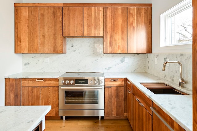 kitchen with stainless steel range, tasteful backsplash, sink, light stone counters, and light wood-type flooring