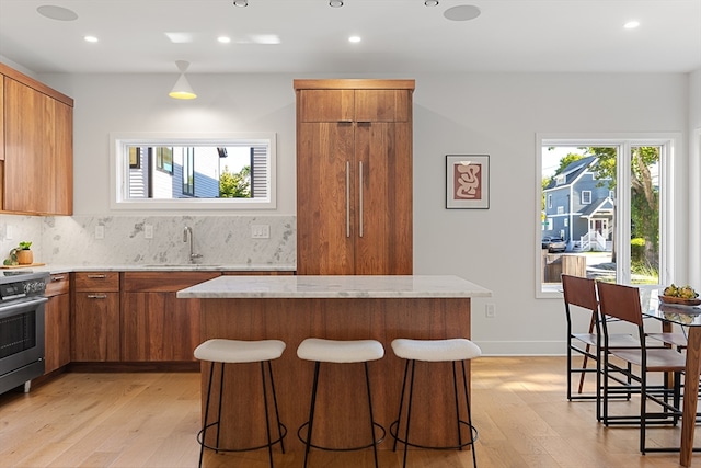 kitchen featuring tasteful backsplash, stainless steel range, a kitchen breakfast bar, and light hardwood / wood-style floors