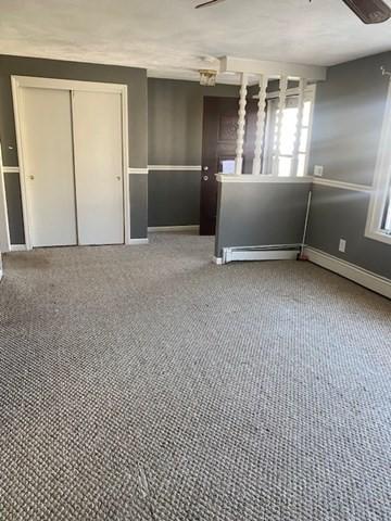 empty room featuring a baseboard radiator, carpet flooring, and baseboards