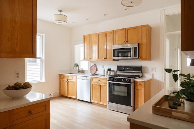 kitchen featuring stainless steel microwave, range with gas cooktop, light wood-style flooring, white dishwasher, and a sink