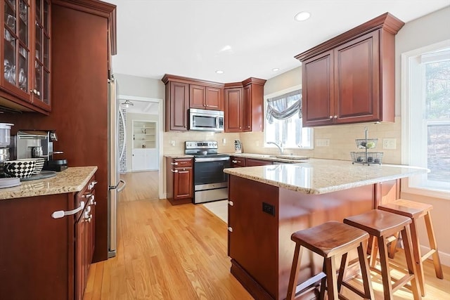 kitchen featuring decorative backsplash, a peninsula, light wood finished floors, and appliances with stainless steel finishes