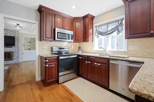 kitchen with light wood-style flooring, a sink, light stone counters, appliances with stainless steel finishes, and a brick fireplace