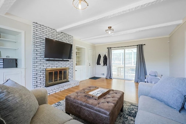 living area featuring built in features, wood finished floors, visible vents, beam ceiling, and a brick fireplace