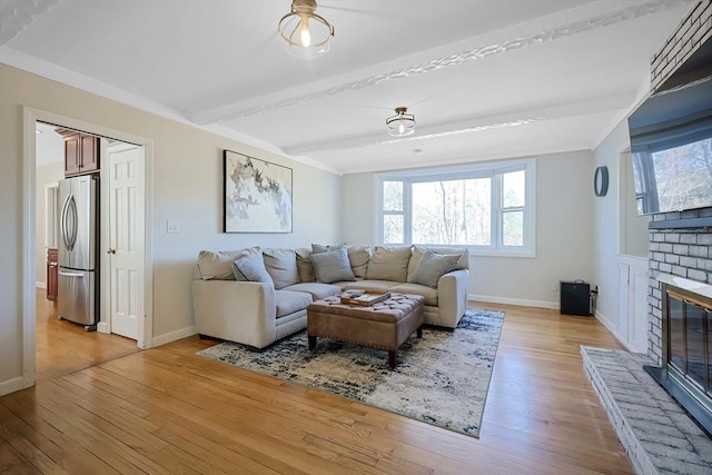 living area featuring beam ceiling, light wood-style flooring, a fireplace, and baseboards