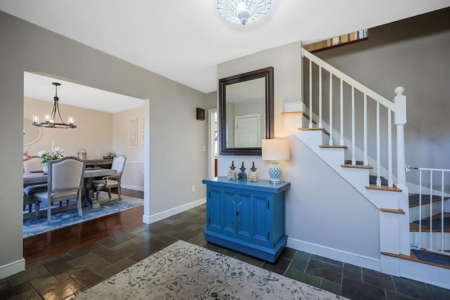 foyer with stone tile floors, a notable chandelier, stairs, and baseboards