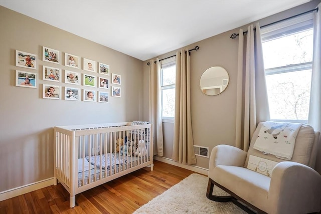 bedroom featuring a nursery area, wood finished floors, visible vents, and baseboards