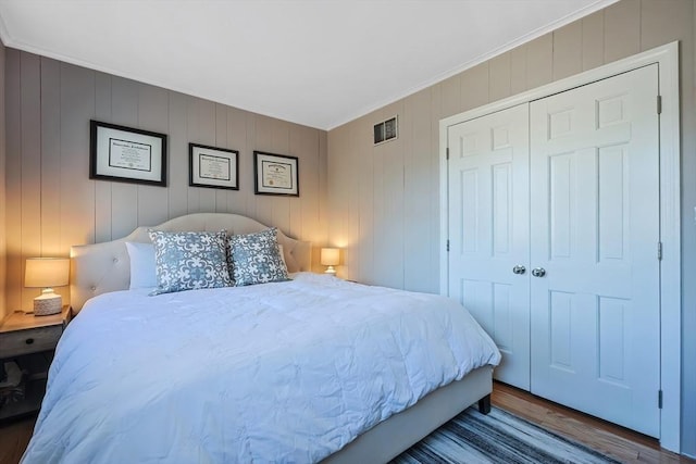 bedroom featuring wood finished floors, visible vents, a closet, and ornamental molding