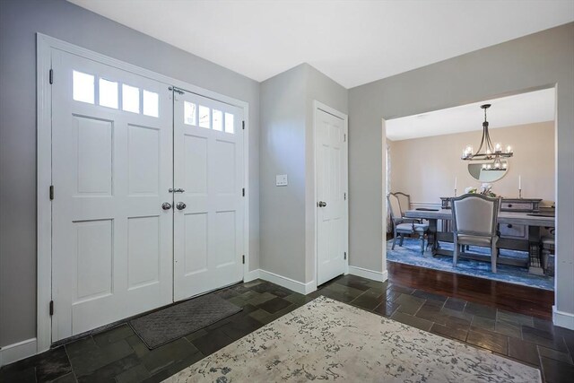 entrance foyer with stone tile floors, baseboards, and an inviting chandelier