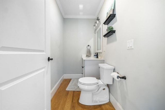 half bath featuring wood finished floors, vanity, baseboards, toilet, and ornamental molding