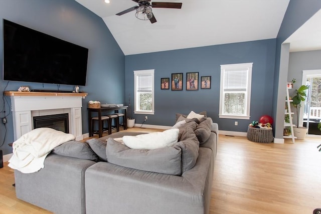 living area featuring ceiling fan, baseboards, lofted ceiling, wood finished floors, and a glass covered fireplace