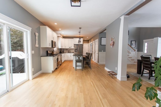 kitchen featuring tasteful backsplash, a breakfast bar, light wood-type flooring, stainless steel appliances, and white cabinetry