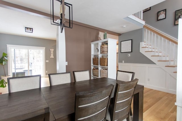 dining room with stairway, a wainscoted wall, wood finished floors, and a decorative wall