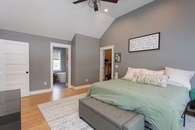 bedroom featuring a walk in closet, baseboards, light wood-type flooring, vaulted ceiling, and ensuite bathroom