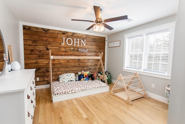 bedroom featuring a ceiling fan, visible vents, baseboards, light wood-style floors, and wood walls