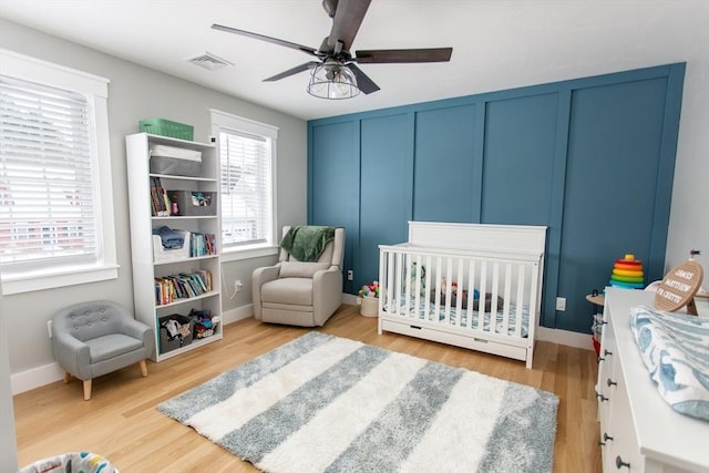 bedroom featuring light wood finished floors, visible vents, a crib, baseboards, and a decorative wall