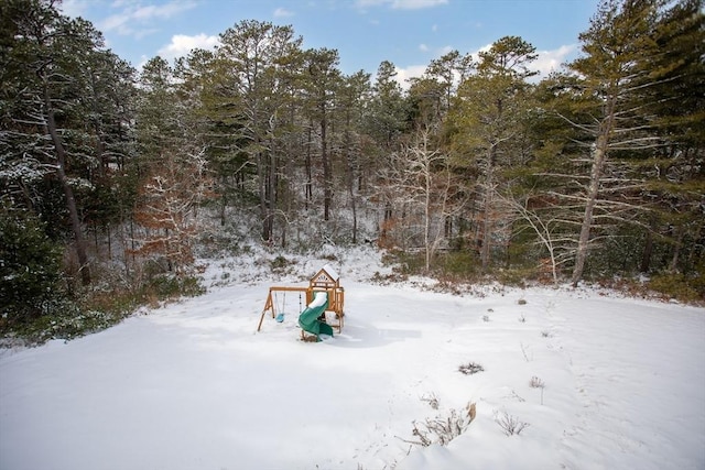 snowy yard featuring a playground and a view of trees