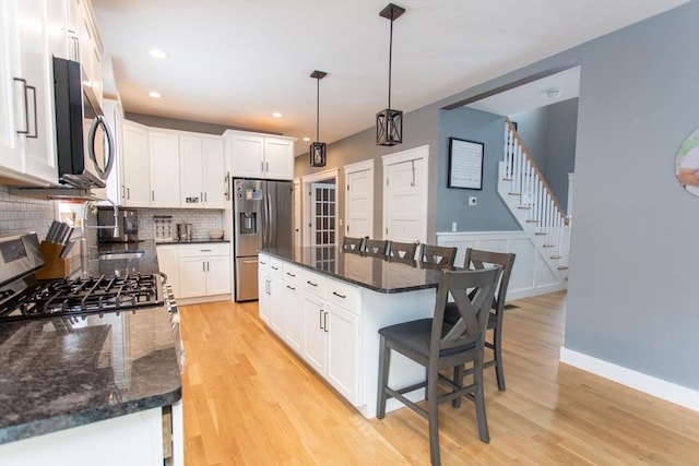 kitchen with light wood-style flooring, white cabinets, appliances with stainless steel finishes, a kitchen breakfast bar, and tasteful backsplash