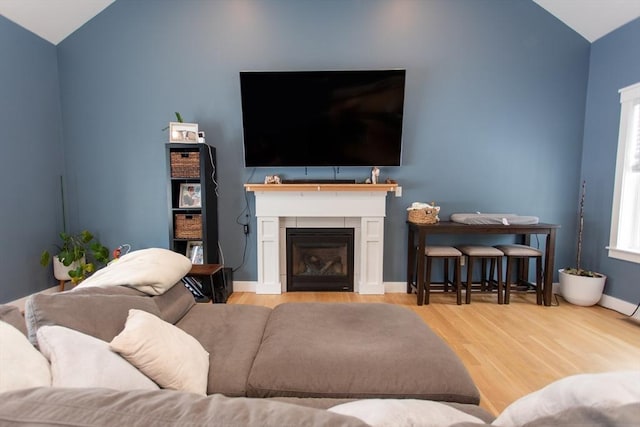 living room featuring a fireplace, wood finished floors, baseboards, and vaulted ceiling