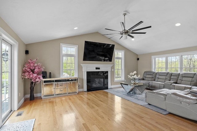 living room with ceiling fan, light wood-style floors, lofted ceiling, a tile fireplace, and baseboards