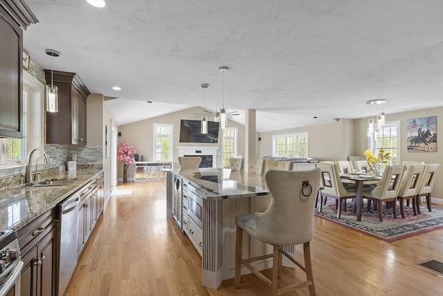 kitchen with open floor plan, a sink, light wood-style flooring, plenty of natural light, and vaulted ceiling