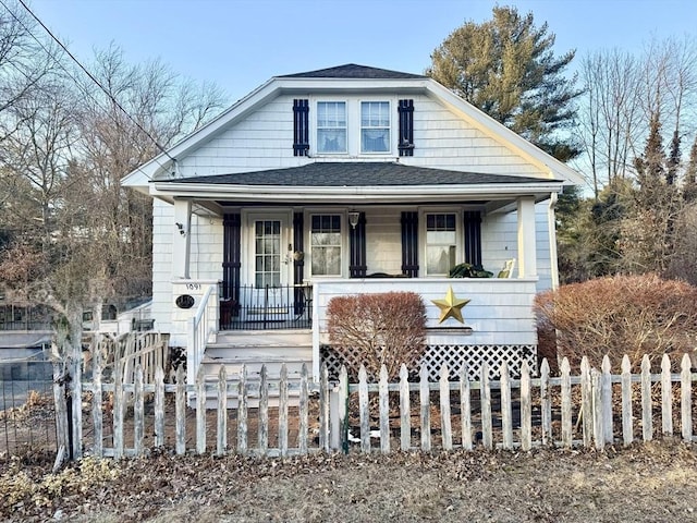 bungalow-style house with covered porch, a fenced front yard, and a shingled roof