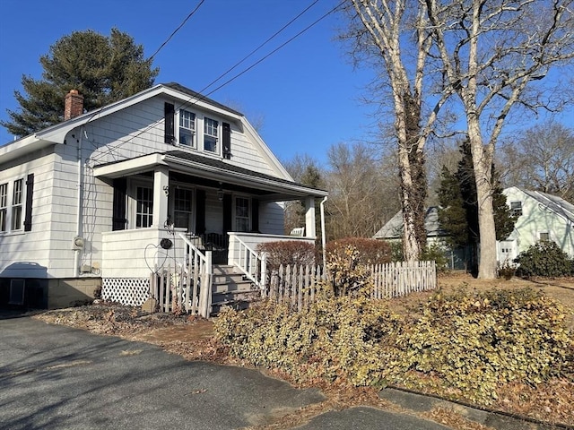 bungalow-style house featuring covered porch, fence, and a chimney