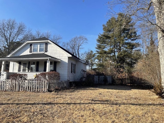 view of property exterior with a yard, covered porch, fence, and a shingled roof