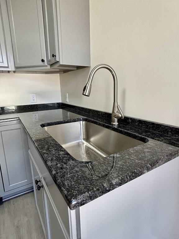 details with light wood-style flooring, dark stone counters, and a sink